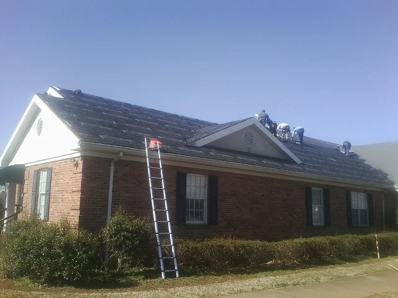 Crew tearing shingles off a brick ranch roof with a ladder set — Metal Roof Repair work by our crew in Corona